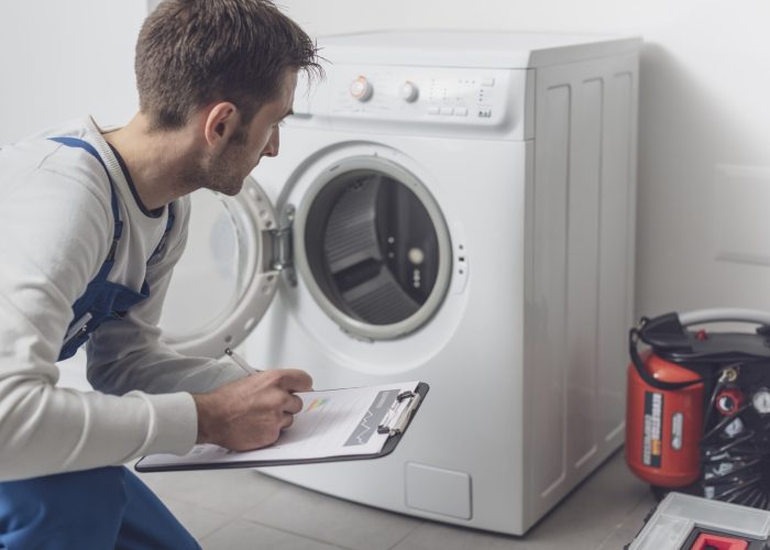 Professional technician checking a washing machine Professional technician checking a washing machine, he is writing on a clipboard